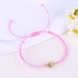 Macro detail of pink braided Hamsa hand bracelet with sparkling crystals on white stand