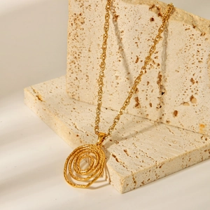 Dettaglio del ciondolo a spirale in acciaio inossidabile 18K su pietra di travertino beige