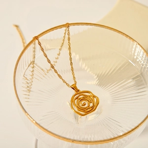 Dettaglio collana con ciondolo rosa traforata placcata oro 18K su bordo di vetro