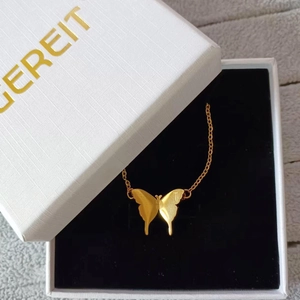 Makroaufnahme eines goldenen Schmetterlingsanhängers mit Gravur T in einer Geschenkbox