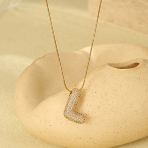 Detailed view of golden letter L pendant necklace with zircon inlay on ceramic stand