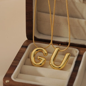 Detail of gold bubble letter G and U pendants with mirror polish on snake chains