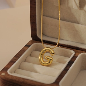 Polished gold bubble letter G pendant necklace displayed in a premium wooden jewelry box