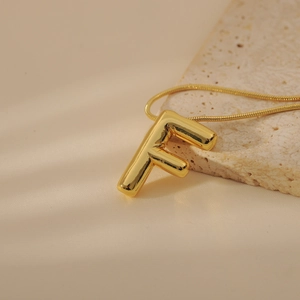 Detail of gold bubble letter F pendant with polished finish on a sleek snake chain