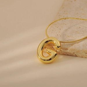 Close-up of golden 3D balloon initial G pendant with sleek snake chain on marble