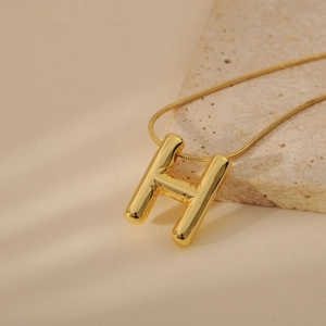 Macro view of gold bubble capital H letter pendant on a sleek snake chain necklace