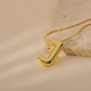 Detail of 3D balloon-style letter J pendant on a gold snake chain over natural stone