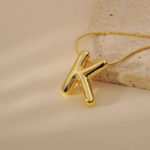 Close-up of golden bubble letter K pendant on snake chain over aesthetic stone background
