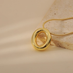 Detail shot of a chunky gold bubble letter pendant on a sleek snake chain over stone
