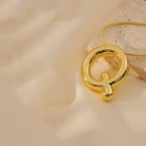 Macro side view of polished gold balloon letter Q pendant on a sleek snake chain