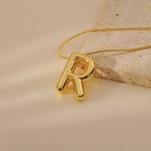 Close-up of golden letter R balloon pendant on a fine snake chain and silk background