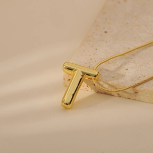 Macro detail of golden 3D bubble letter T pendant on a sleek snake chain necklace
