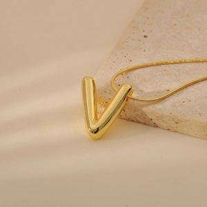 Macro detail of a 3D gold V-letter bubble pendant with a sleek snake chain on stone