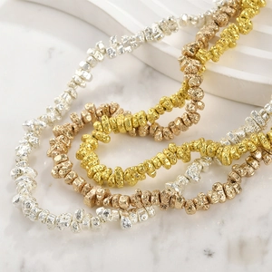 Gold and silver irregular metallic volcanic stone beaded necklaces on white marble surface