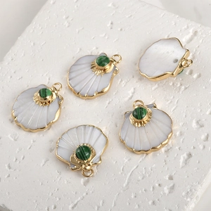 Detailed close-up of shell-shaped gold plated pendants with inlaid green stones on stone