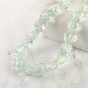 Macro detail of iridescent mint green heart beads with holographic glitter texture