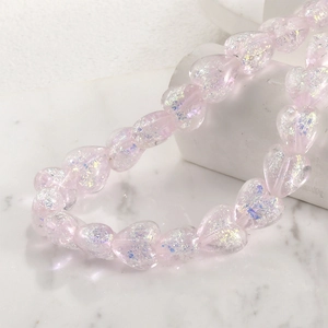 Close-up of translucent pink heart beads with iridescent glitter on marble background