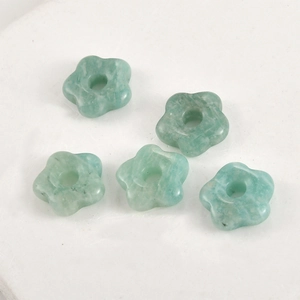 Close-up of five flower-shaped light green natural stone beads with central drill holes