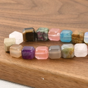 Mixed natural gemstone cube beads including tiger eye and amethyst on a wooden tray