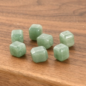 Close-up of seven green crystal cube beads with center drill holes on wood surface