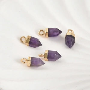Détail de cinq prismes hexagonaux en améthyste violette avec embouts dorés sur plateau blanc