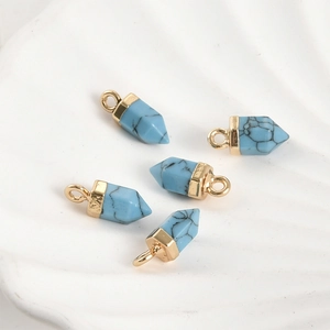 Détail de cinq pendentifs hexagonaux en turquoise avec calottes dorées sur plateau blanc