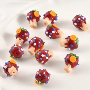 Detailed view of handmade red glass mushroom beads with blue spots for DIY jewelry