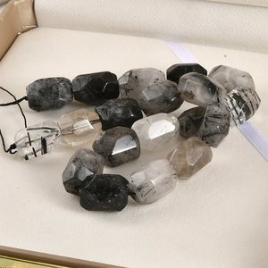 Macro shot of faceted black rutilated quartz tube beads on a white display tray