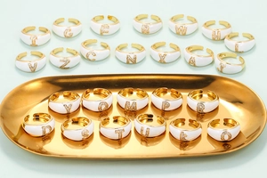 Adjustable gold rings with white enamel and micro-pave letter accents in a metal tray