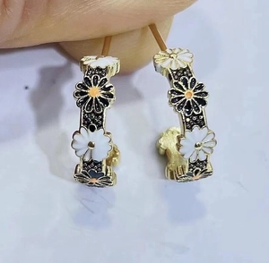 Golden C-shaped hoop earrings featuring black and white daisy enamel patterns