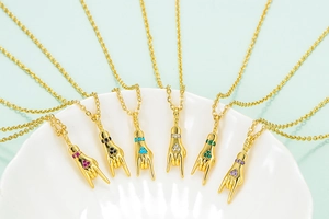 Set of six gold-plated hand gesture pendants with colorful stones on a textured tray