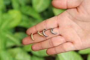 Orecchini a cerchio intrecciati minimalisti in oro e argento su sfondo naturale