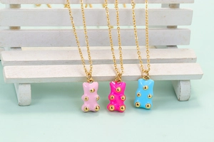 Three colorful enamel bear pendants with gold studs hanging on a white wooden chair prop