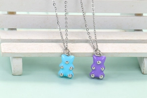 Close-up of light blue and purple enamel bear pendants on silver chains with prop bench