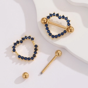 Macro detail of a 18K gold-plated heart nipple ring with blue zircon inlay on white board