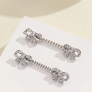 Detailed close-up of silver bow nipple rings with sparkling zircon inlay on white stand