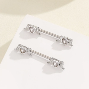 Detail of silver nipple rings featuring feather wings and heart-shaped zircon stones
