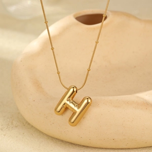 Close-up of golden bubble letter H pendant with delicate gold snake chain texture