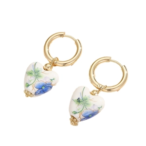 Pendientes de corazón dorados con colgantes de cerámica de flores azules en fondo blanco