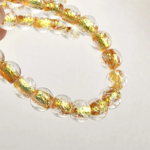 Dettaglio macro di perle di vetro trasparente con scaglie di foglia d'oro per gioielli fai da te