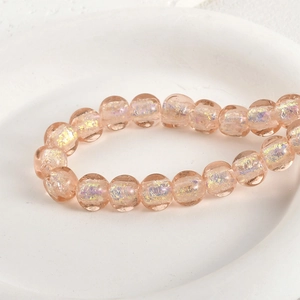 Macro shot of iridescent peach glass beads with gold foil texture on a white ceramic tray