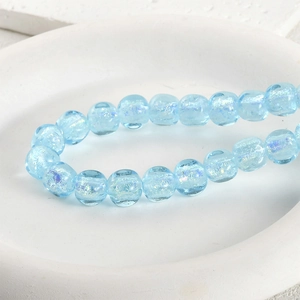 Close-up of light blue translucent glass beads with internal glitter on a ceramic plate