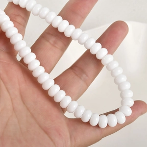 Vista macro de cuentas de vidrio blanco de 5x8mm en la mano para escala y textura