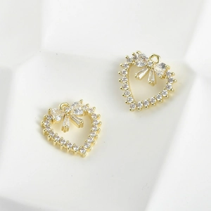 Detailed close-up of 14k gold plated heart pendants with zircon bowknots on white surface