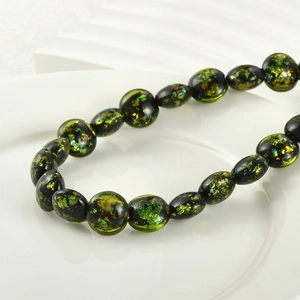 Macro shot of dark green glass beads with gold foil flakes on a white ceramic tray