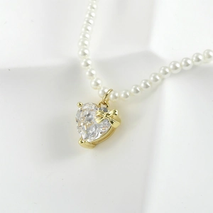 Detail of heart-shaped zircon pendant with gold bow accent on a pearl necklace