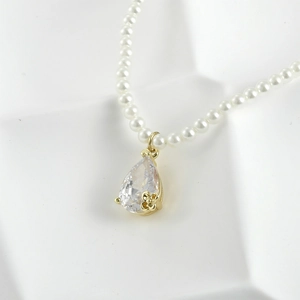 Detail of 14K gold plated teardrop zircon pendant on a dainty white pearl necklace