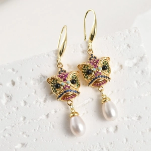 Detalle de pendientes de león danzante bañados en oro 18k con cristales y perla