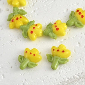 Macro detail of yellow glass tulip beads with red dots and green leaf for DIY jewelry