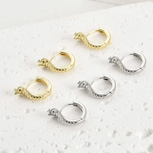 Vue détaillée des boucles d'oreilles serpent dorées et argentées avec yeux en zircon vert